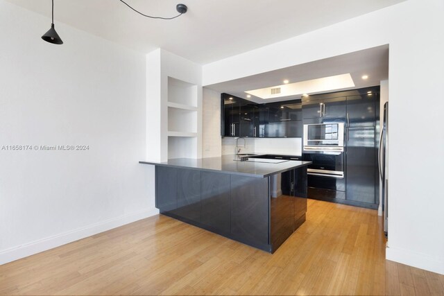 kitchen with appliances with stainless steel finishes, kitchen peninsula, light wood-type flooring, and decorative light fixtures