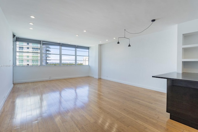 unfurnished living room featuring light wood-type flooring, a healthy amount of sunlight, and built in features