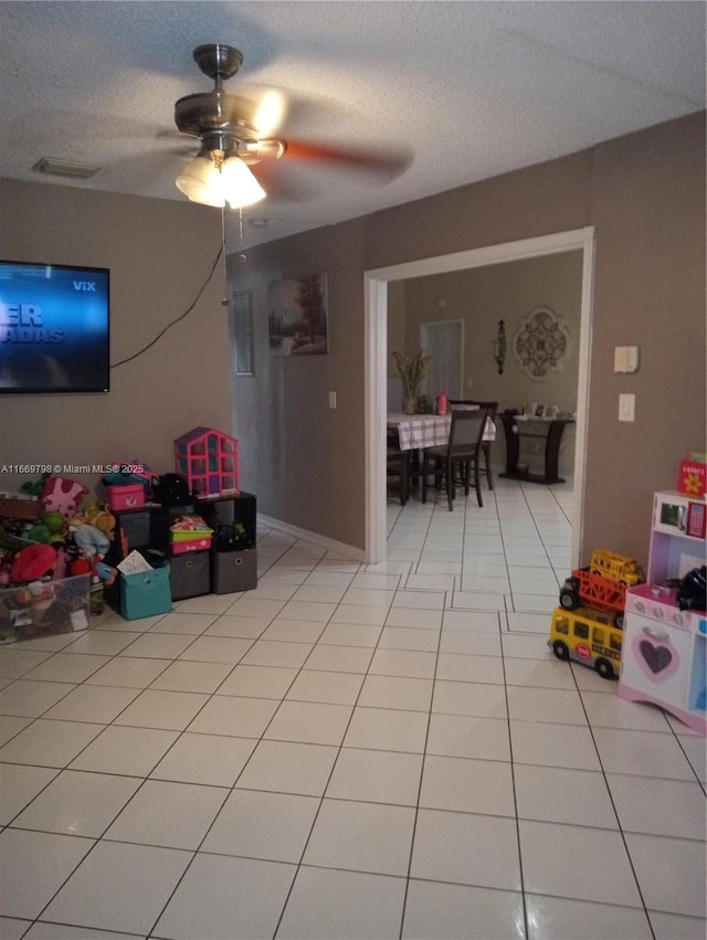 recreation room featuring ceiling fan, light tile patterned flooring, and a textured ceiling