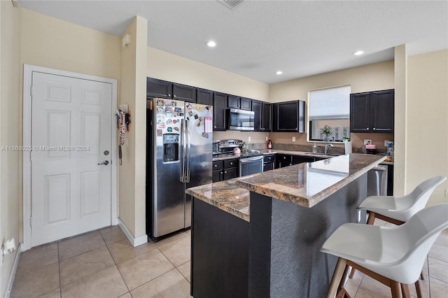 kitchen with stainless steel appliances, a kitchen breakfast bar, light stone countertops, a textured ceiling, and light tile patterned floors