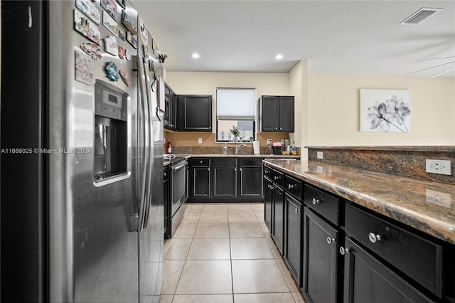 kitchen with light tile patterned flooring, stainless steel appliances, a textured ceiling, dark stone countertops, and ceiling fan