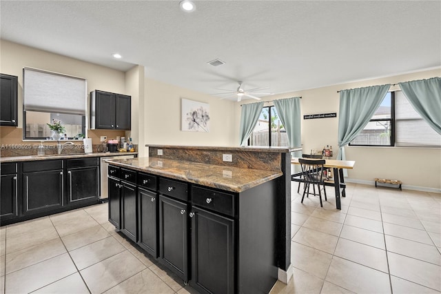 kitchen with light tile patterned flooring, stone countertops, ceiling fan, a textured ceiling, and a kitchen island