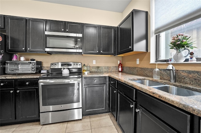 kitchen with stainless steel appliances, sink, stone counters, and light tile patterned floors