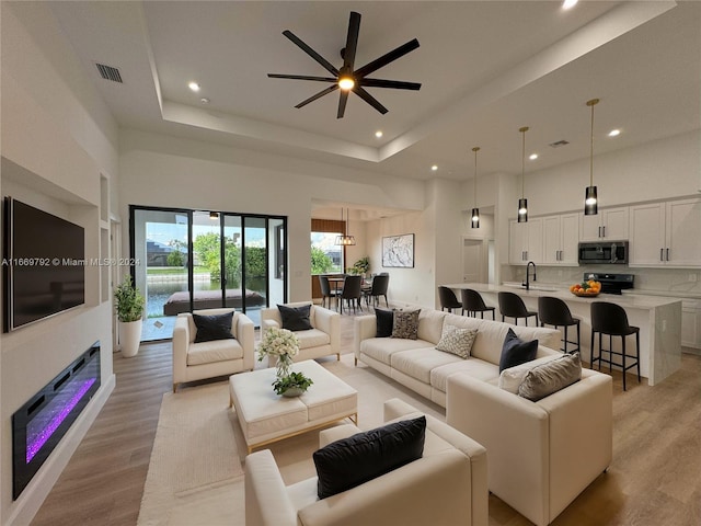 living room featuring a towering ceiling, ceiling fan, a raised ceiling, and light wood-type flooring