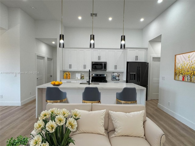 kitchen with pendant lighting, white cabinets, a center island with sink, black appliances, and a towering ceiling