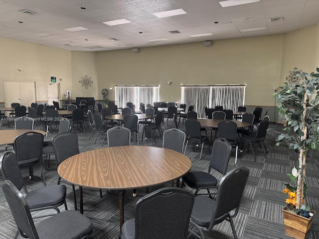 dining space featuring visible vents, a high ceiling, a drop ceiling, and carpet