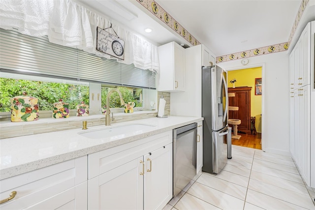 kitchen featuring white cabinets, light tile patterned flooring, sink, appliances with stainless steel finishes, and light stone countertops