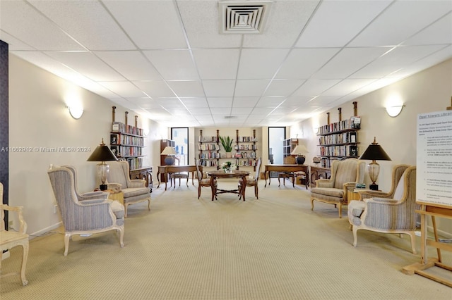 living area with a drop ceiling and carpet