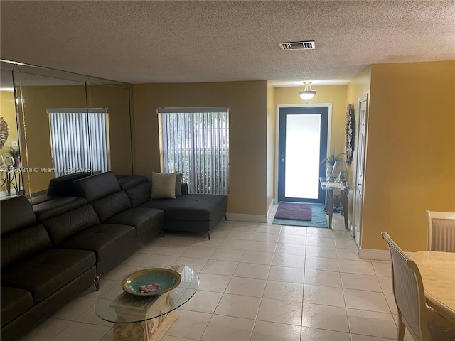 living room with a textured ceiling, light tile patterned flooring, visible vents, and baseboards