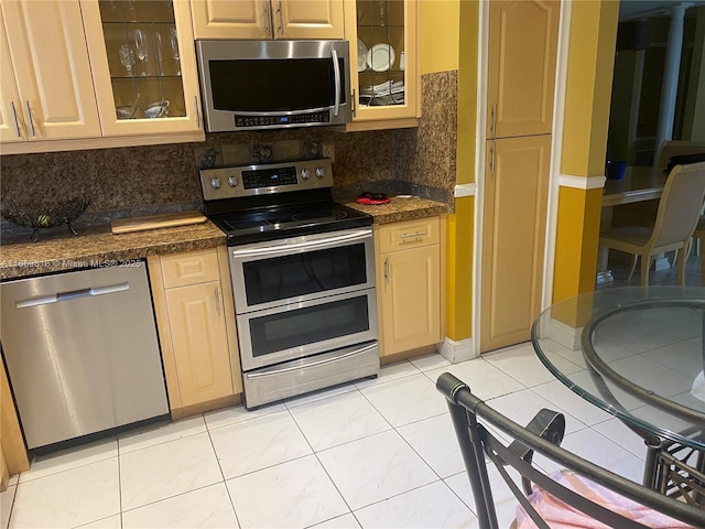 kitchen featuring light tile patterned floors, appliances with stainless steel finishes, backsplash, and glass insert cabinets