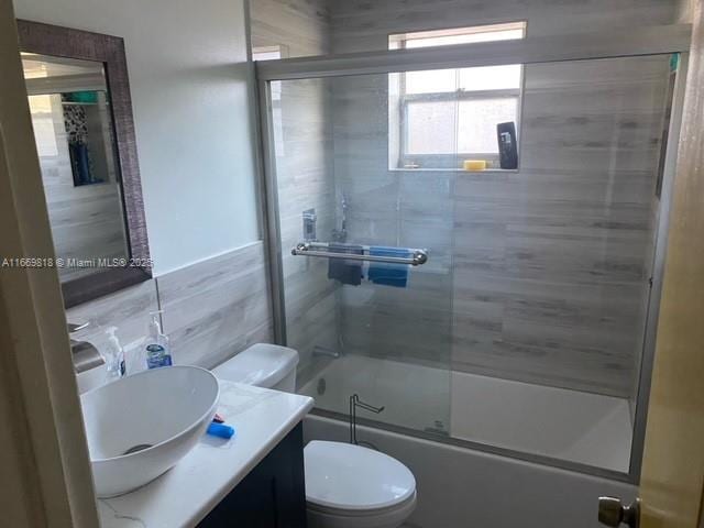 bathroom featuring tile walls, combined bath / shower with glass door, vanity, and toilet