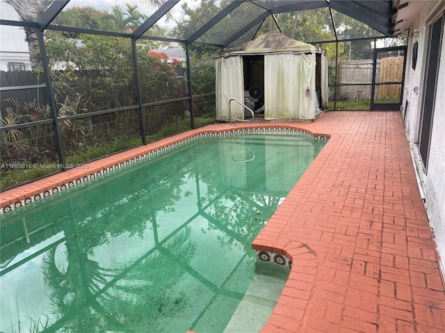 view of swimming pool featuring glass enclosure, an outdoor structure, fence, a storage unit, and a patio area