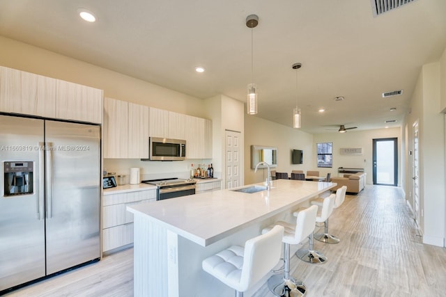 kitchen featuring hanging light fixtures, light hardwood / wood-style floors, stainless steel appliances, a center island with sink, and sink