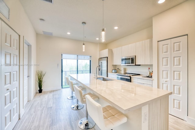 kitchen featuring stainless steel appliances, hanging light fixtures, a kitchen island with sink, and a breakfast bar area