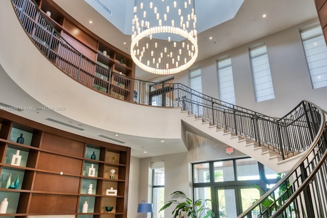 stairs with a notable chandelier, a towering ceiling, and a healthy amount of sunlight