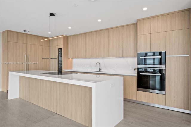 kitchen featuring black electric cooktop, hanging light fixtures, a kitchen island with sink, light brown cabinetry, and double oven