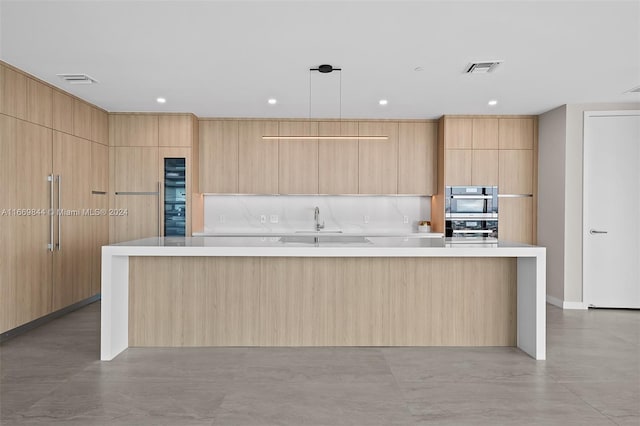 kitchen featuring light brown cabinets, a large island with sink, and decorative light fixtures