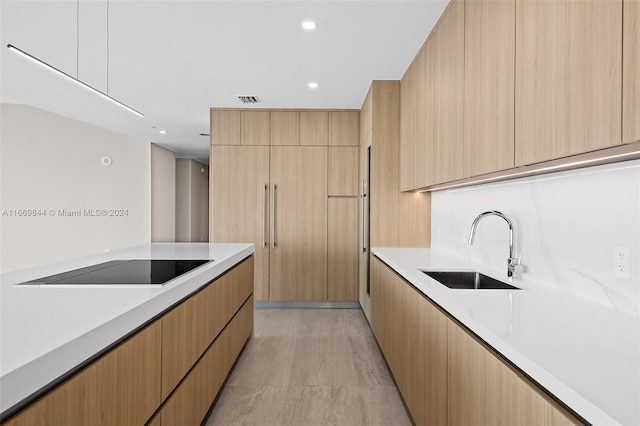 kitchen with light brown cabinets, light wood-type flooring, sink, and black electric stovetop