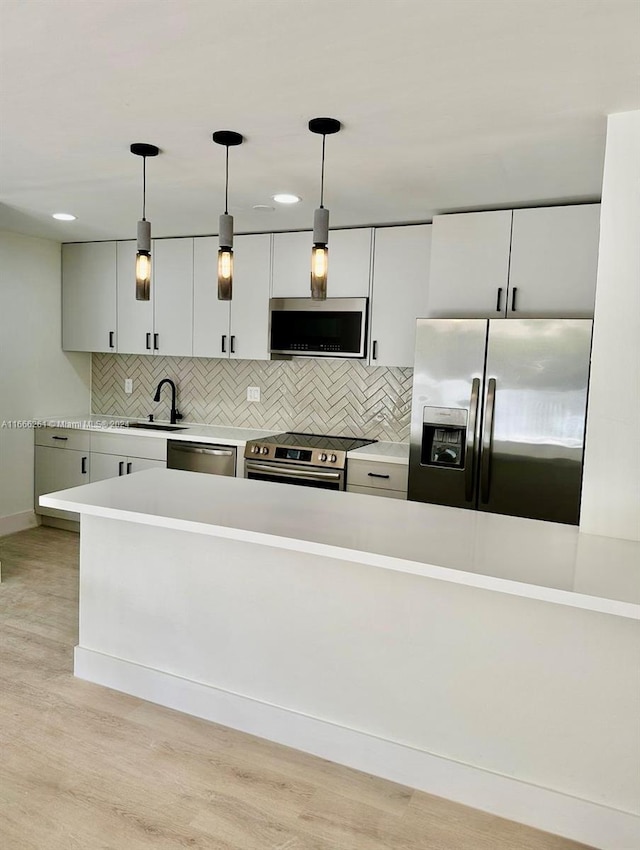 kitchen with decorative light fixtures, stainless steel appliances, tasteful backsplash, and light hardwood / wood-style flooring