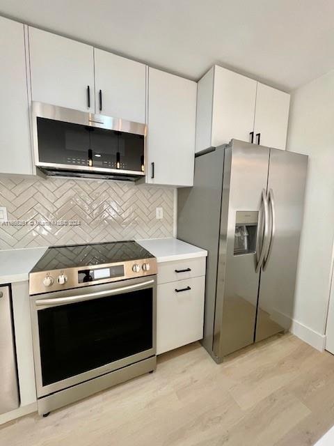 kitchen featuring light hardwood / wood-style floors, white cabinetry, stainless steel appliances, and tasteful backsplash