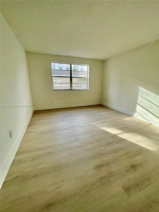 empty room with a textured ceiling and light hardwood / wood-style flooring