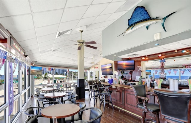 interior space featuring a drop ceiling, indoor bar, ceiling fan, and dark wood-type flooring