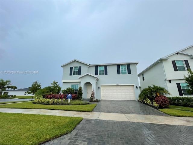 traditional-style home featuring a front lawn, decorative driveway, an attached garage, and stucco siding