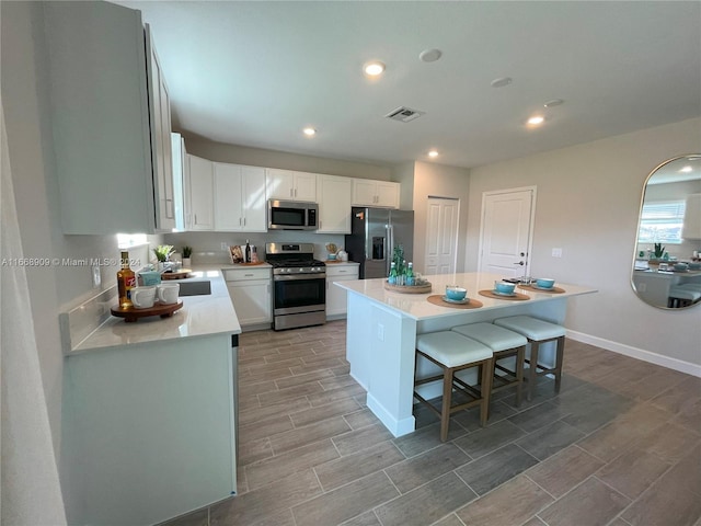 kitchen with appliances with stainless steel finishes, a kitchen bar, a kitchen island, and white cabinetry