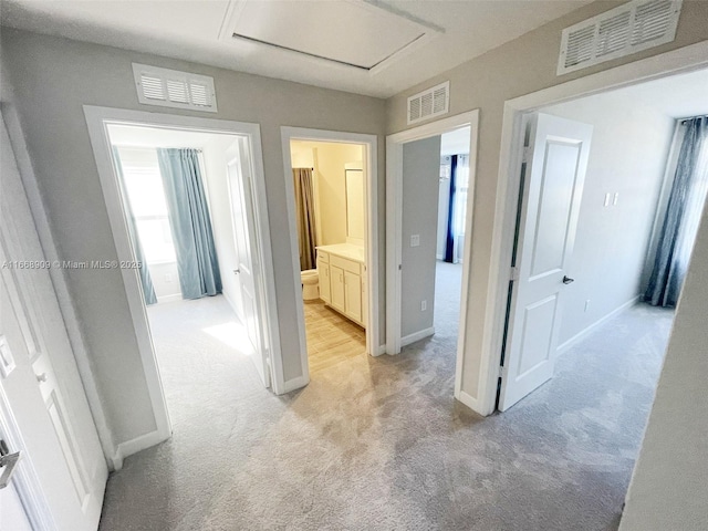 hall featuring visible vents, baseboards, and light colored carpet