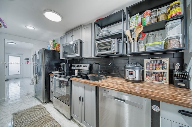 kitchen featuring sink, wooden counters, gray cabinetry, appliances with stainless steel finishes, and decorative backsplash