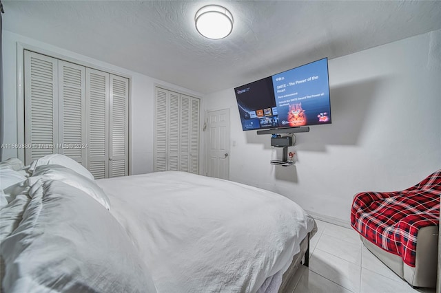 bedroom featuring multiple closets, a textured ceiling, and light tile patterned floors