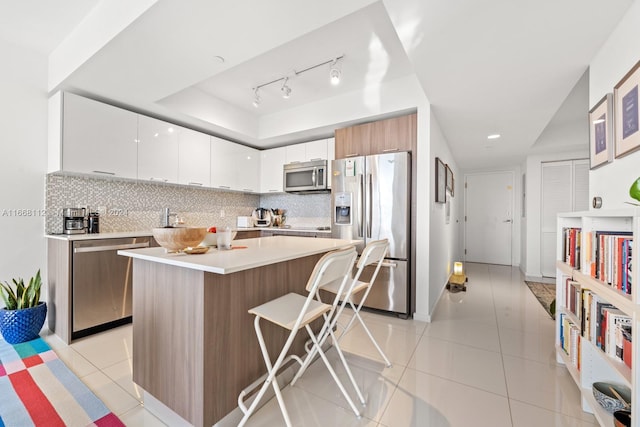 kitchen featuring a kitchen island, a kitchen breakfast bar, stainless steel appliances, white cabinetry, and tasteful backsplash