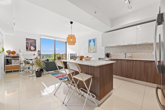 kitchen featuring hanging light fixtures, tasteful backsplash, light tile patterned floors, white cabinetry, and stainless steel refrigerator