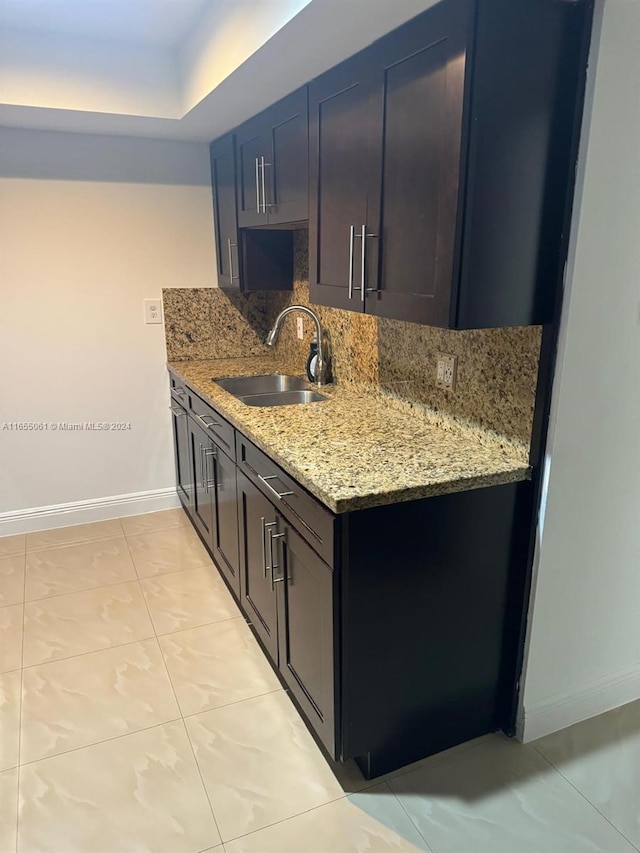 kitchen with dark brown cabinetry, light tile patterned flooring, sink, tasteful backsplash, and light stone countertops