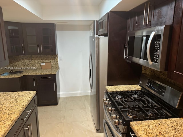 kitchen featuring light stone countertops, dark brown cabinets, appliances with stainless steel finishes, and light tile patterned flooring