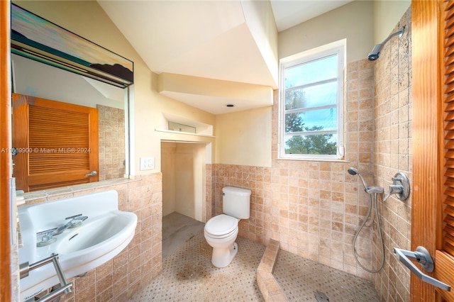 bathroom featuring toilet, a tile shower, tile patterned floors, tile walls, and vaulted ceiling