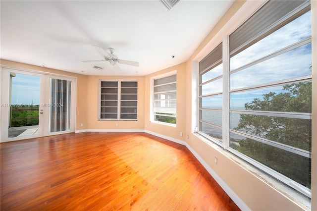 unfurnished sunroom featuring a water view, ceiling fan, and french doors