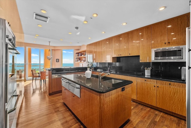 kitchen featuring a water view, light hardwood / wood-style floors, stainless steel microwave, and a kitchen island with sink