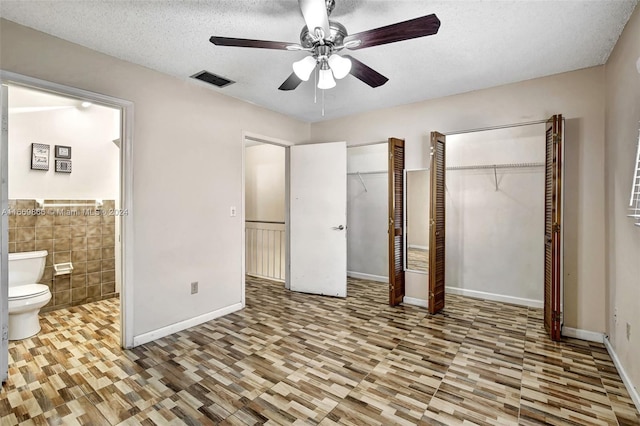 unfurnished bedroom featuring tile walls, a textured ceiling, ensuite bathroom, two closets, and ceiling fan