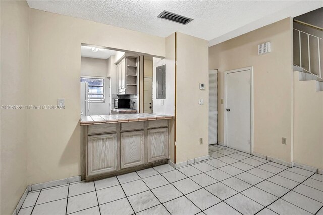 kitchen featuring a textured ceiling, tile countertops, electric panel, and light tile patterned floors