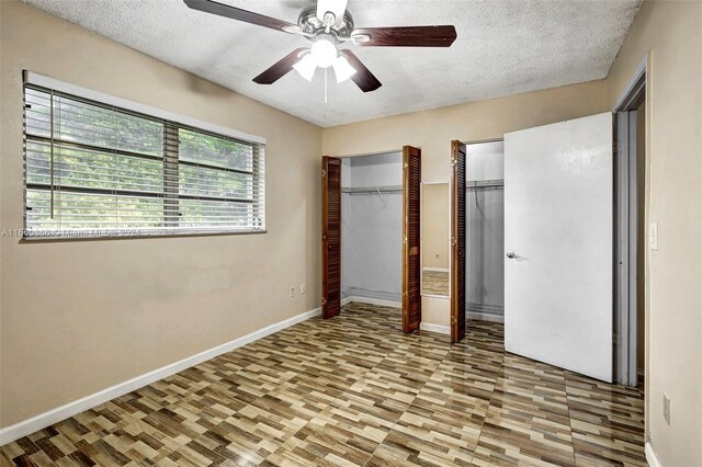 unfurnished bedroom with ceiling fan, hardwood / wood-style flooring, two closets, and a textured ceiling