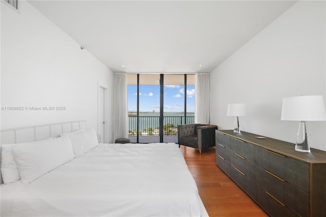 bedroom with access to exterior, a water view, hardwood / wood-style floors, and floor to ceiling windows