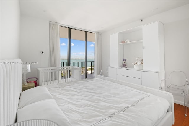 bedroom with wood-type flooring, access to outside, a water view, radiator, and a wall of windows