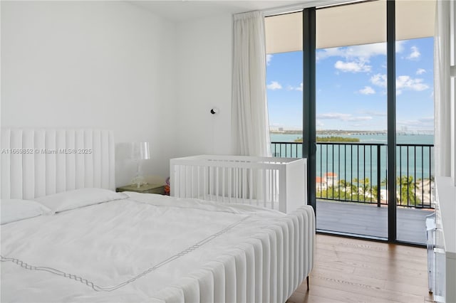 bedroom featuring access to exterior, a water view, floor to ceiling windows, and light hardwood / wood-style flooring