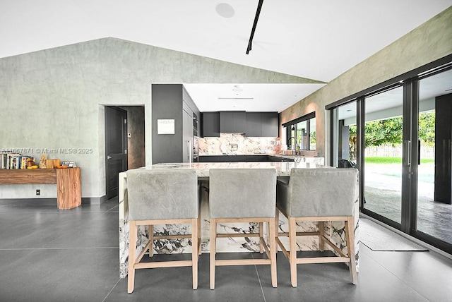 kitchen featuring sink, a kitchen breakfast bar, light stone countertops, vaulted ceiling, and kitchen peninsula