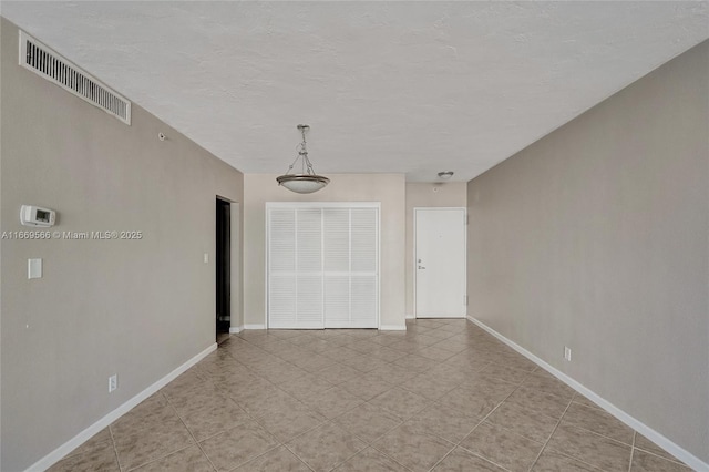 unfurnished room featuring a textured ceiling, light tile patterned floors, visible vents, and baseboards