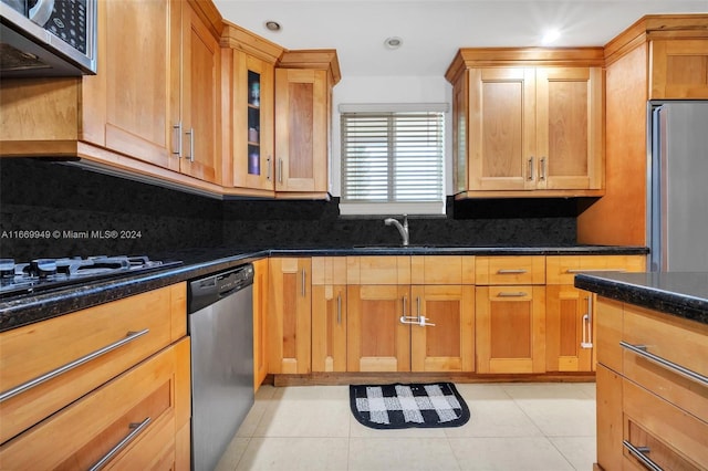 kitchen featuring light tile patterned floors, glass insert cabinets, a sink, appliances with stainless steel finishes, and backsplash