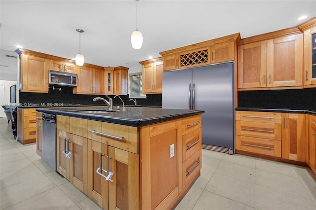 kitchen featuring an island with sink, sink, tasteful backsplash, decorative light fixtures, and appliances with stainless steel finishes