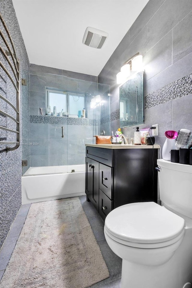 full bathroom featuring tile walls, shower / bath combination with glass door, tile patterned floors, vanity, and toilet