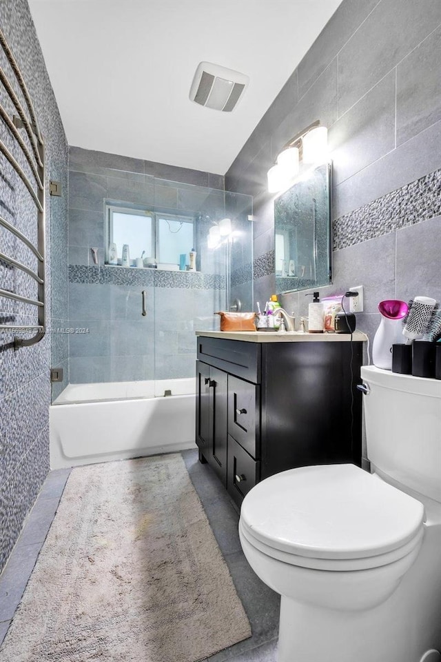 bathroom with tile walls, vanity, bath / shower combo with glass door, toilet, and visible vents